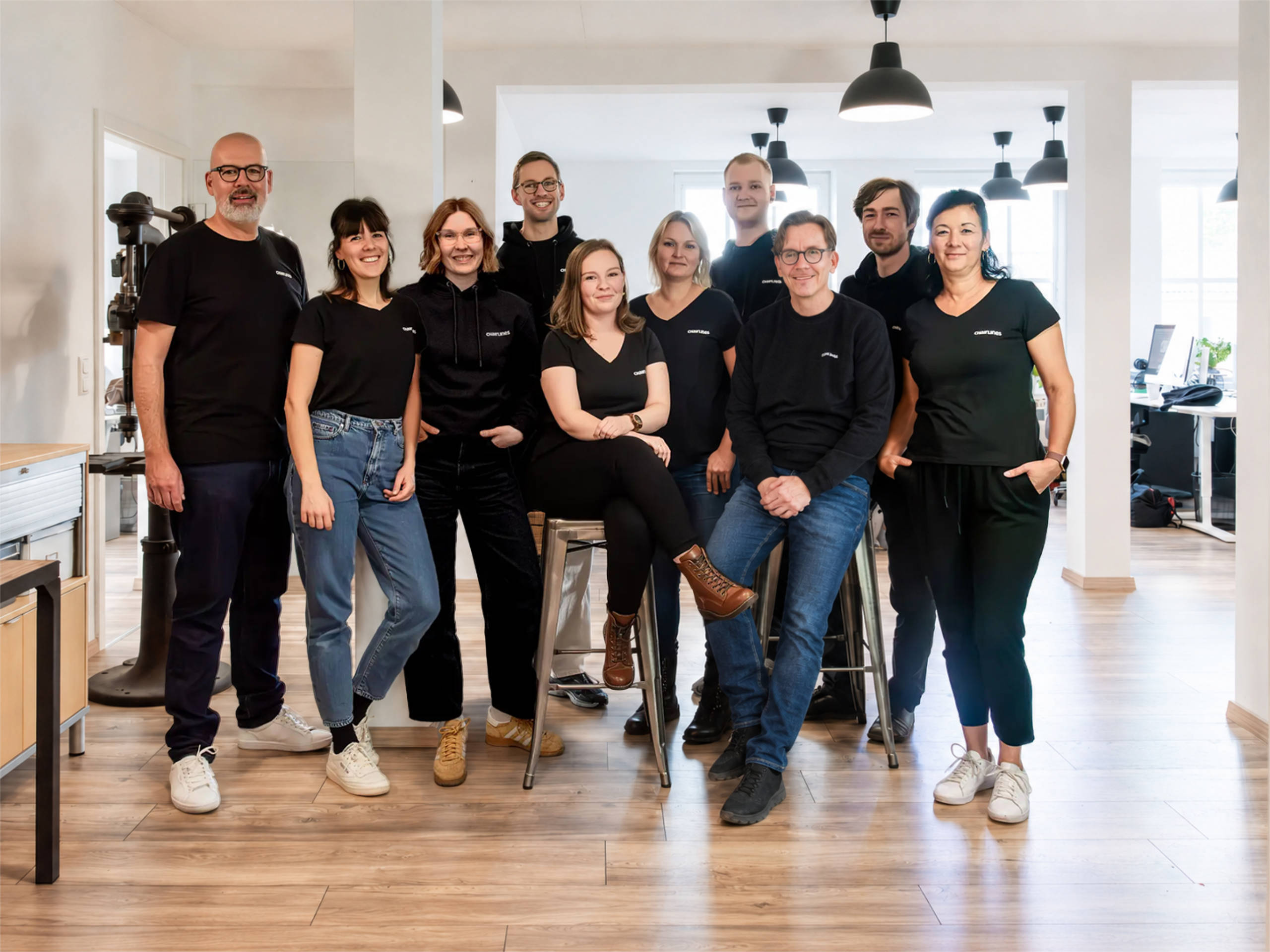 chairlines_crew-2026 Team der strategischen Designagentur chairlines aus der Lausitz, stehend und sitzend als Gruppe in den Agenturräumen in der alten Bürstenfabrik in Spremberg